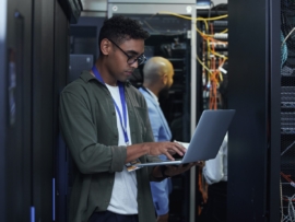 Ttwo male IT support agents working together in a dark network server room.
