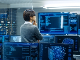 A person standing in an office surrounded by screens showing different data and data visualizations.